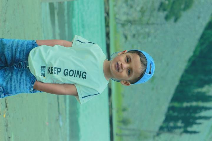 Portrait of a young boy wearing a cap standing by a turquoise mountain river.