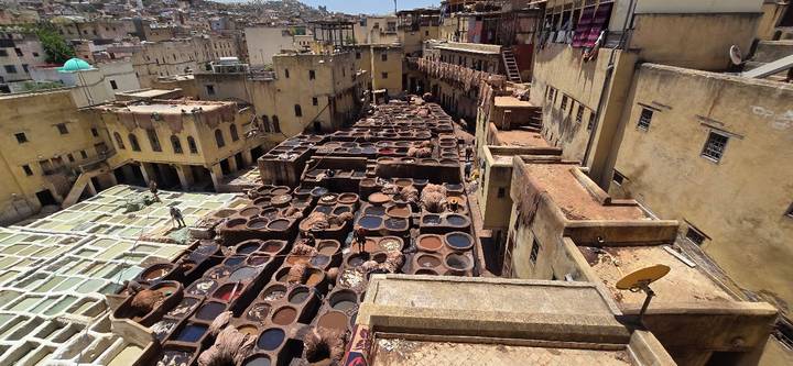 Elevated view of Fes’s ancient tannery filled with multicolored dye vats surrounded by yellowed buildings.