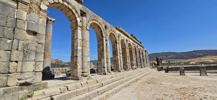 Row of ancient Roman arches standing amid stone ruins under a cloudless blue sky at Volubilis.