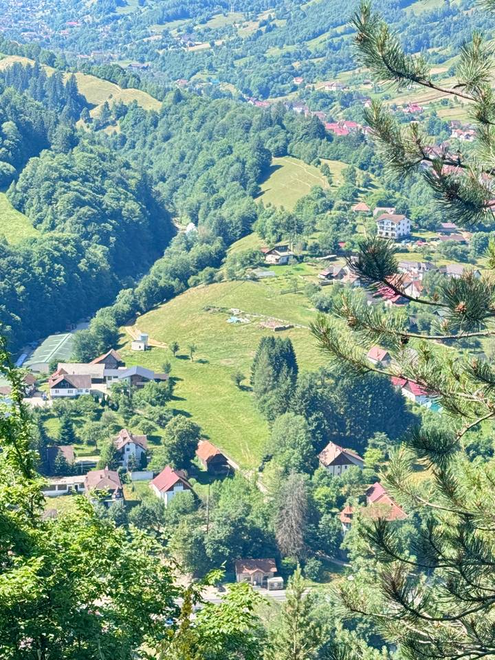 Elevated view over a rural Romanian valley dotted with houses and forested hillsides.