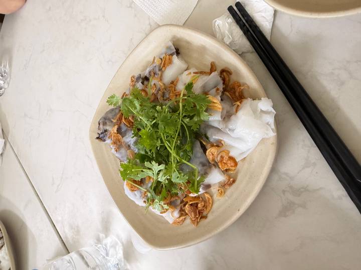 Plate of steamed rice rolls filled with mushroom, topped with fried shallots and fresh cilantro.