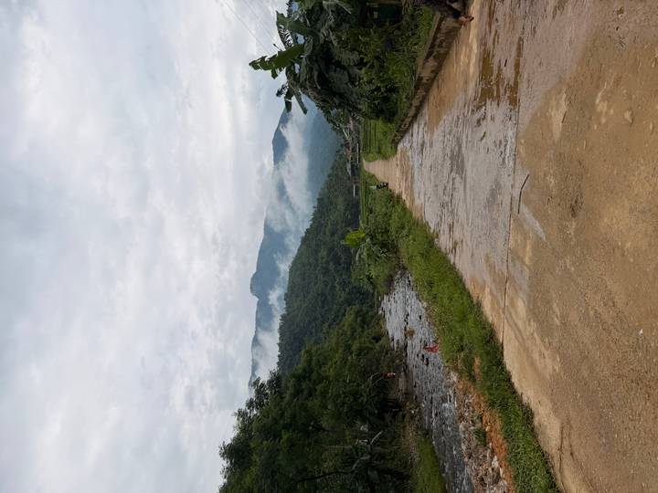 Misty mountains loom beyond a rural path beside a small river in northern Vietnam countryside.