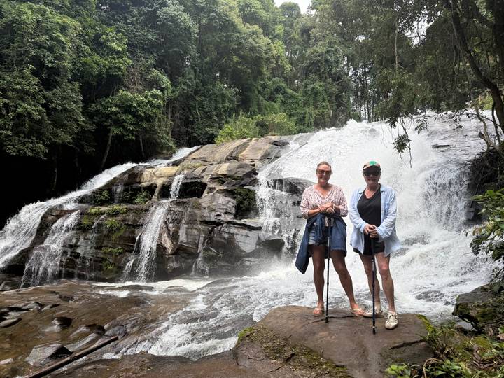 Two women posing on rocks in front of a cascading forest waterfall