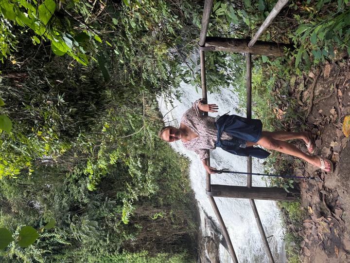 Woman leaning on wooden railing beside rushing waterfall in lush forest