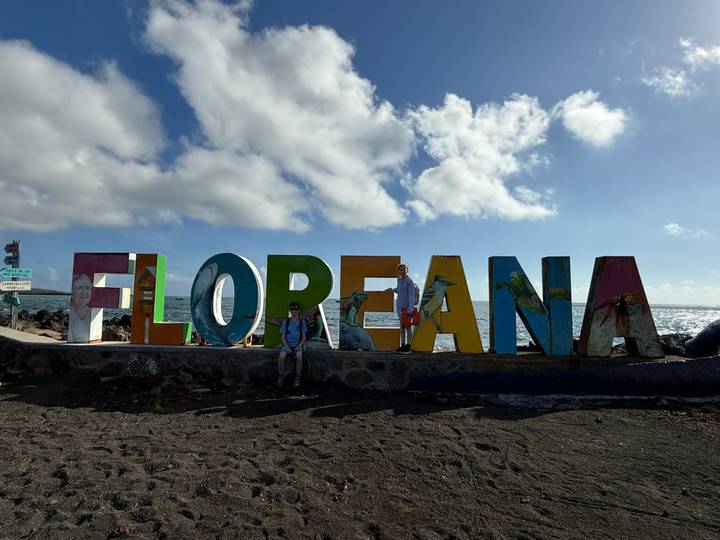 Traveler posing in front of large colorful FLORANA sign on volcanic sand beach with bright sun