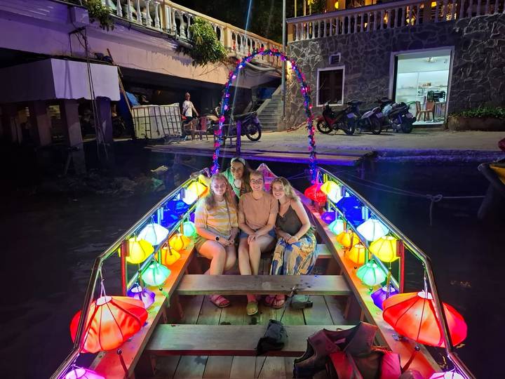 Four women seated in a lantern-lit boat glowing with multicolored lights on a canal at night