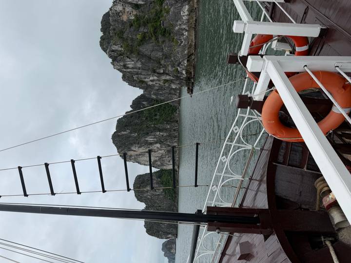 View from a wooden cruise deck of towering limestone karsts rising from emerald waters in Halong Bay