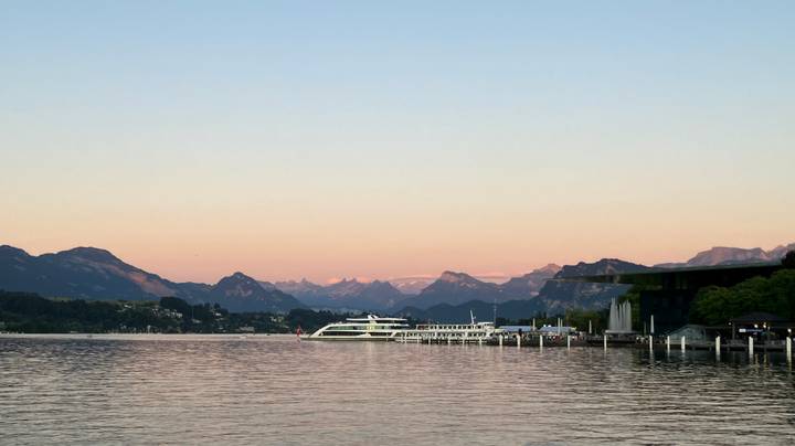 Serene lake scene at dusk with a cruise boat docked against Alpine peaks bathed in pastel sunset hues