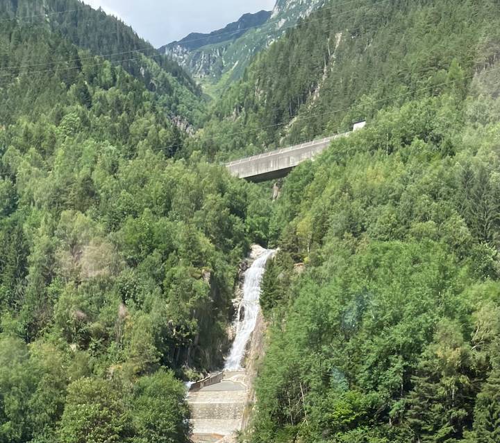 Forest-clad valley with a narrow waterfall dropping beneath a concrete bridge high above the trees