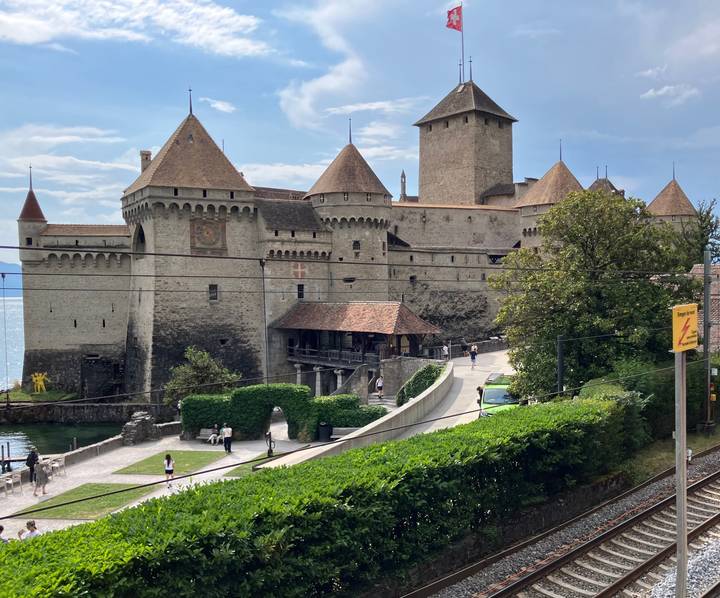 Medieval lakeside Château de Chillon with towers and ramparts, visitors walking along the shore road