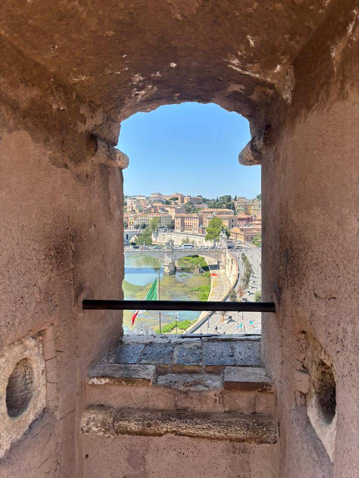 Panoramic Rome cityscape framed by stone walls of Castel Sant’Angelo, with river, bridge and flag below