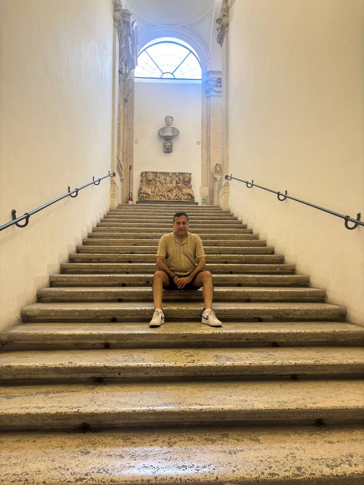 Man seated midway on a grand stone stairway inside a historic Italian building