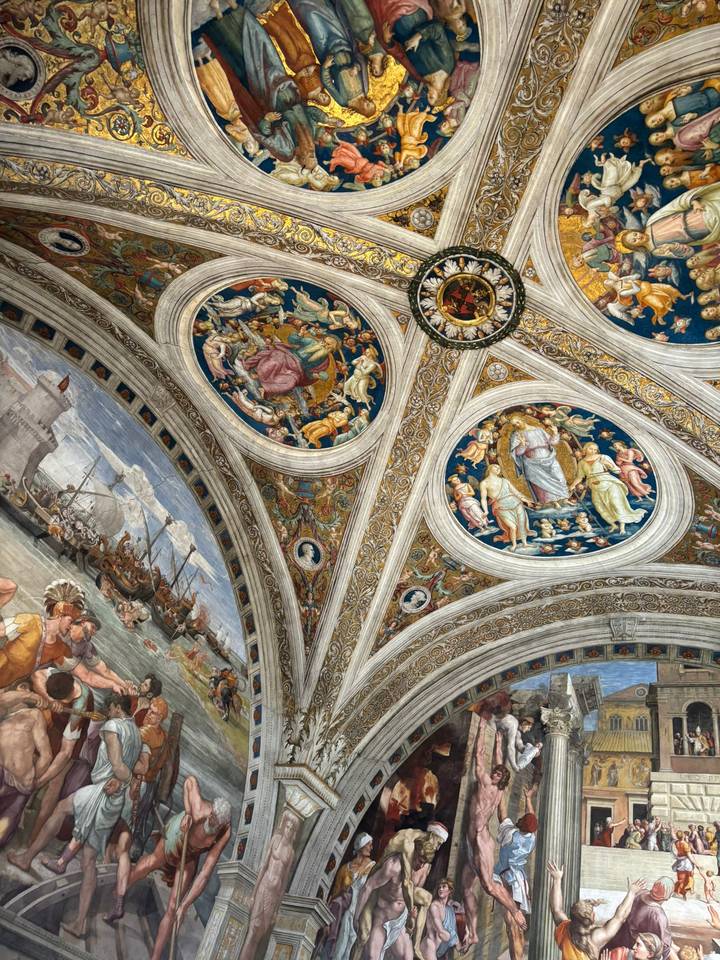 Ornate Renaissance frescoes and gilded decoration cover arched ceilings inside a grand Vatican gallery.