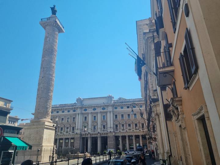 Ancient column and elegant façade rise against a clear blue Roman sky.