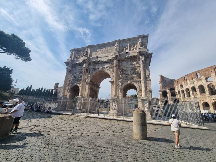 The Arch of Constantine stands majestically beside the Colosseum as visitors gather around.