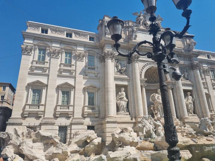 Baroque façade of the Trevi Fountain with marble figures framed by an ornate lamppost.
