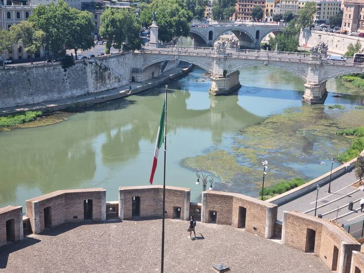 Aerial view from Castel Sant’Angelo of the Tiber River and stone bridge with Italy’s flag flying.