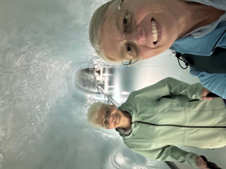 Two smiling women walk through an illuminated ice tunnel inside a glacier attraction.