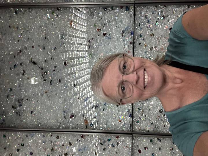 Smiling woman taking a selfie in front of a sparkling crystal-covered wall indoors.