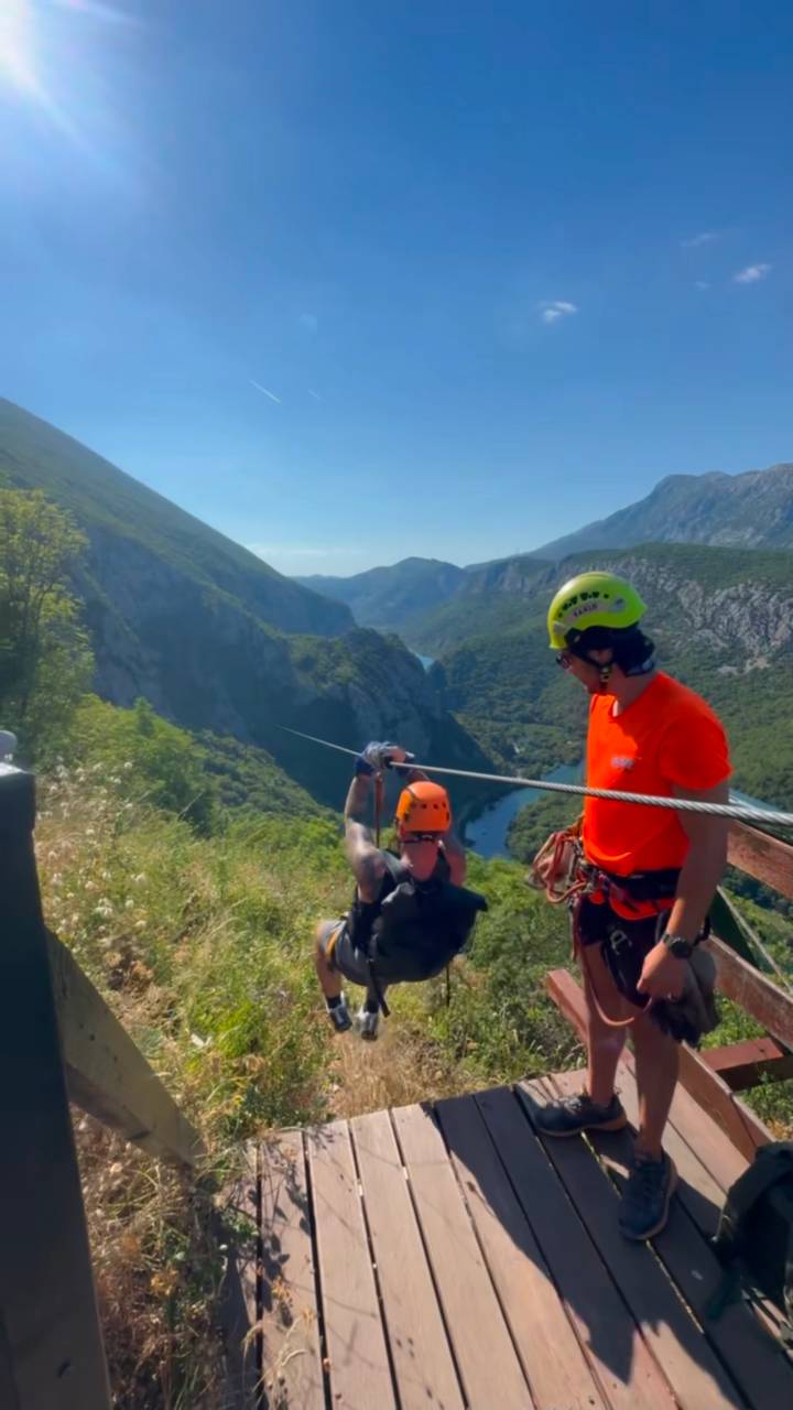 Adventurers prepare to zip-line over a deep green canyon with helmets and harnesses.