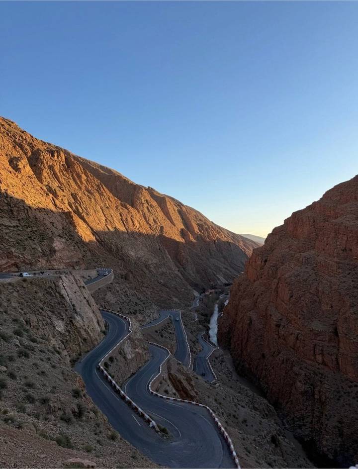 Dramatic canyon with winding mountain road and river below, bathed in late-day light casting long shadows.