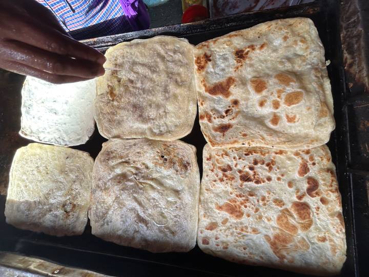 Close-up of square flatbreads sizzling on a griddle while a hand drizzles honey over them.