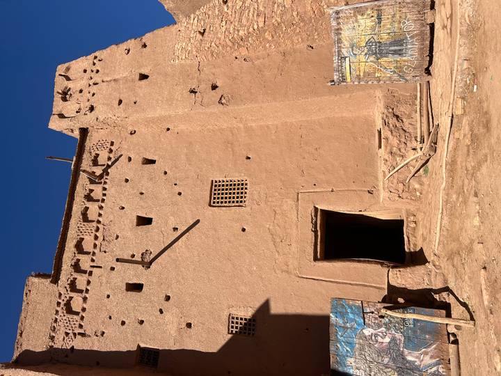 Tall earthen kasbah wall with small windows and decorative crenellations against a deep blue sky.