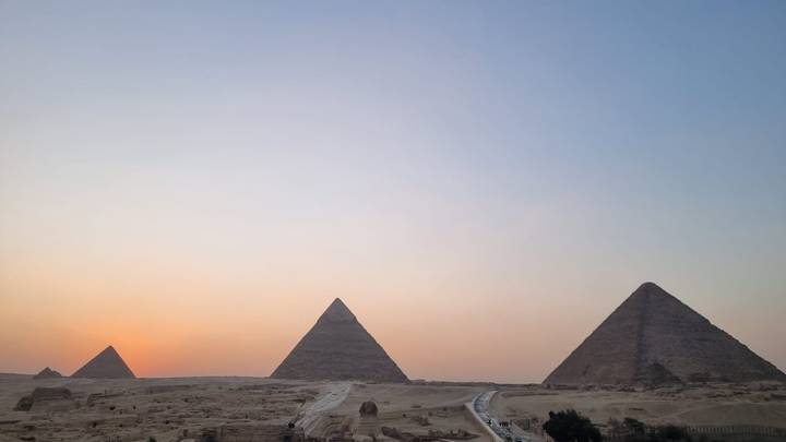 Three pyramids of Giza line the horizon with a subtle orange sunset glow.