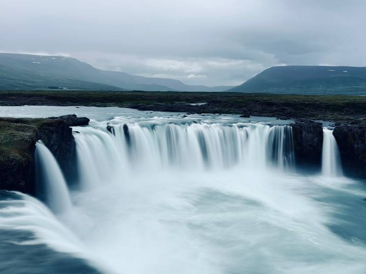 Long-exposure photograph of a wide waterfall cascading into a misty gorge under cloudy skies.