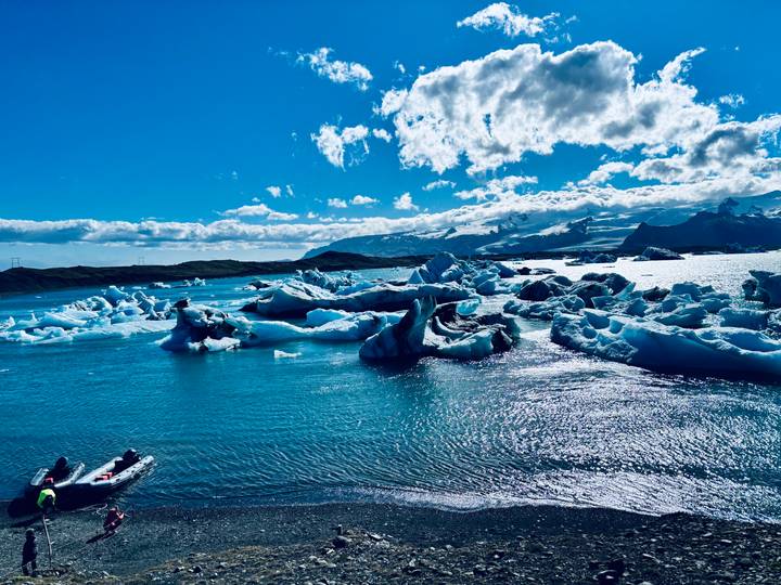 Bright blue glacial lagoon filled with sculpted icebergs under a sunny sky.