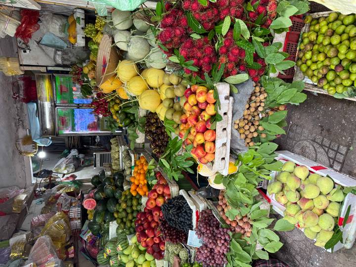 Abundant display of fresh fruits including rambutan, apples, melons, longan and watermelon at an open-air market.