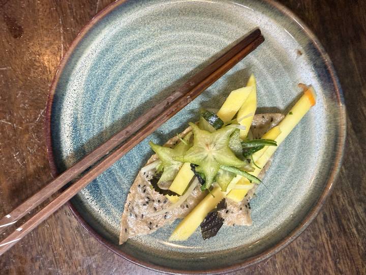A small artistic tasting plate topped with starfruit, mango slices and sesame crepe beside wooden chopsticks.