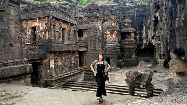 Traveler posing amid the intricately carved stone temples and pillars of the Ellora Caves complex.