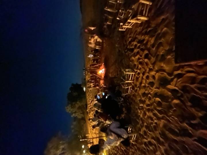 Nighttime desert campfire gathering with people seated in a circle on sand around glowing flames.