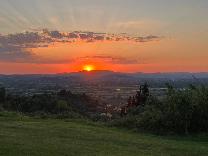 Vibrant sunset over a wide Greek valley with mountains silhouetted against an orange sky
