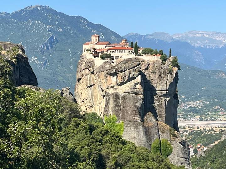 Monastery perched atop a dramatic rock pillar with green mountains in the background at Meteora