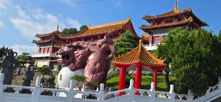 Colorful traditional temple with large red guardian lion statue set against a bright sky