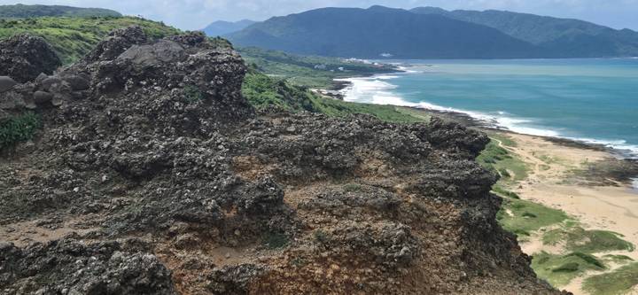 Rugged volcanic rock landscape overlooking turquoise sea and sandy shoreline