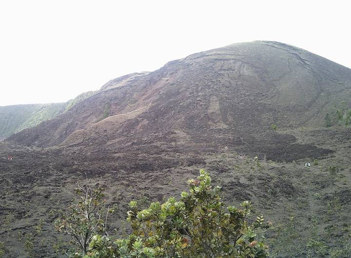 Dark volcanic cone covered in lava rocks under an overcast sky