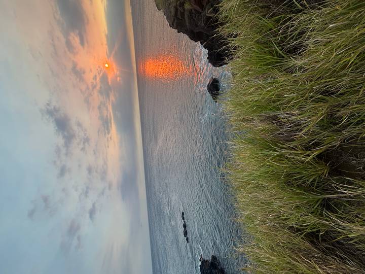 Fiery orange sun sets over calm ocean waters casting a glowing reflection and pastel sky.