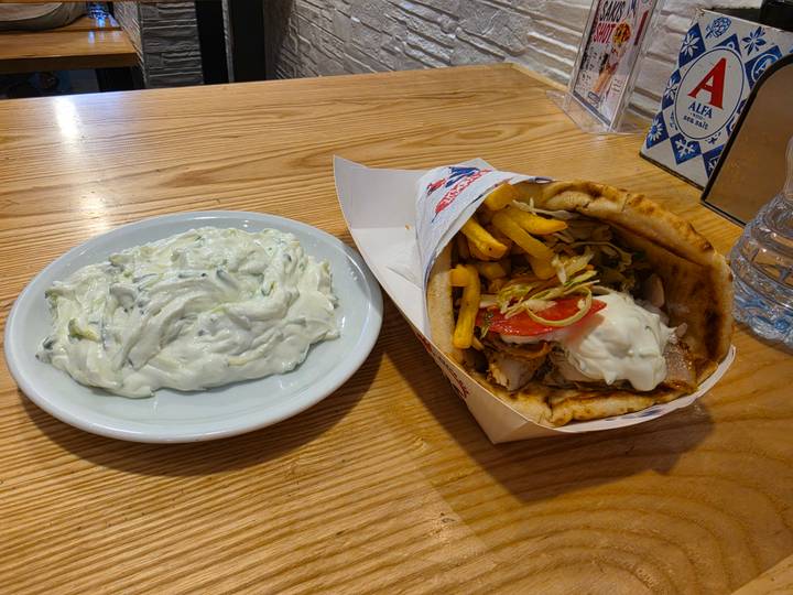 Gyro sandwich with fries and side plate of creamy tzatziki on wooden table.
