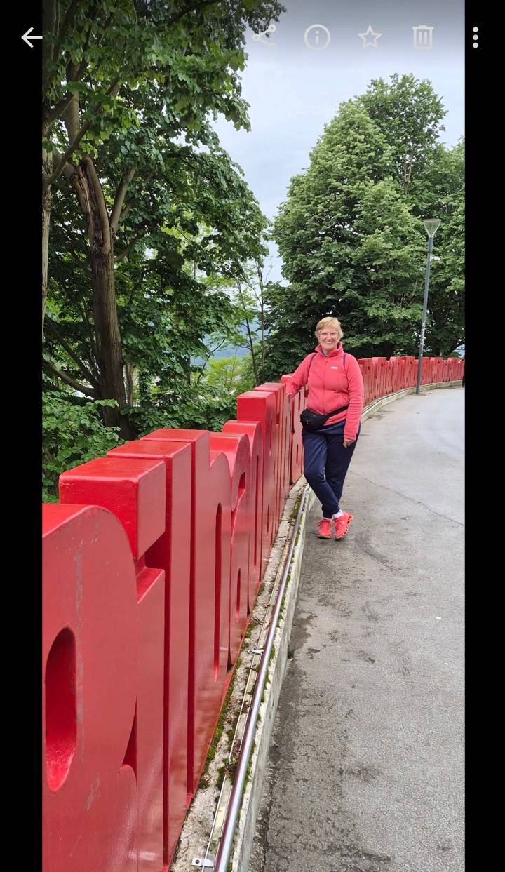 Traveller in a pink jacket stands beside large red sculptural letters lining a curved viewpoint path.