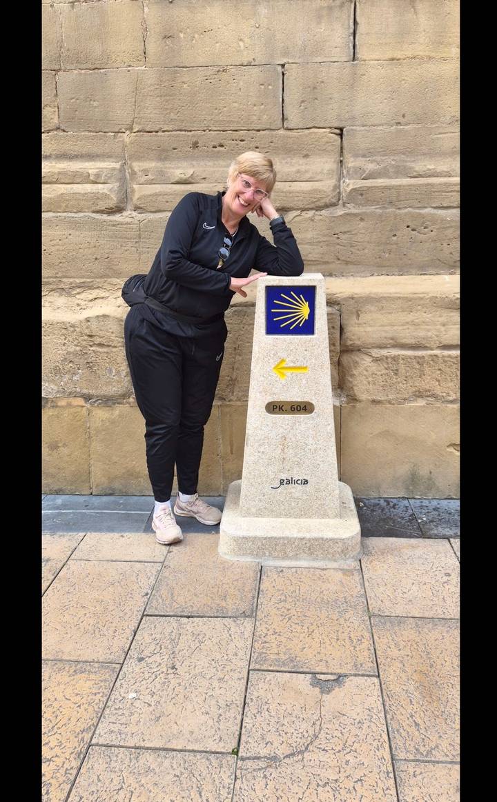 Traveller points to a Camino de Santiago milestone with a yellow arrow and scallop shell emblem.