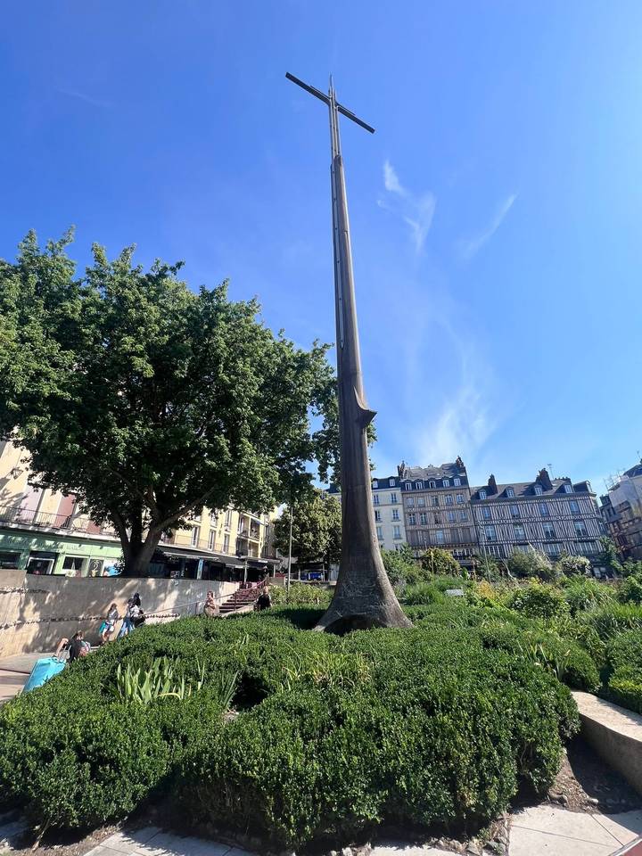 Tall modern monument in city square with traditional timbered buildings behind