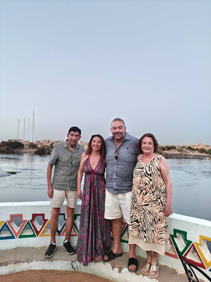 Four friends posing by a wide Nile riverside at dusk with low hills behind.