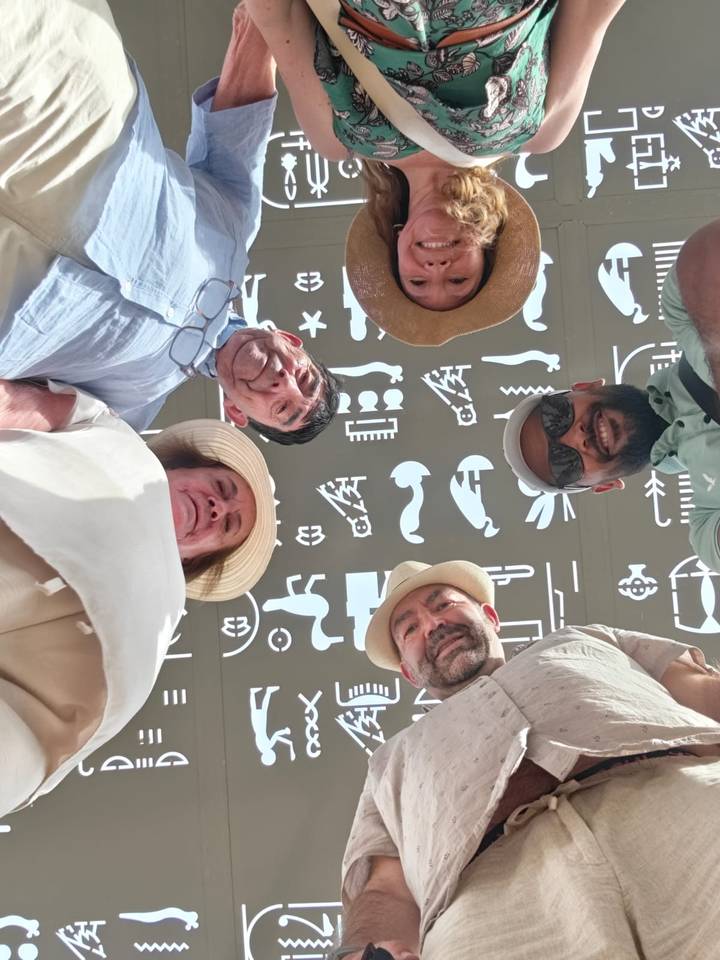 Creative upward shot of five travellers forming a circle, with Egyptian hieroglyphics on a ceiling above.