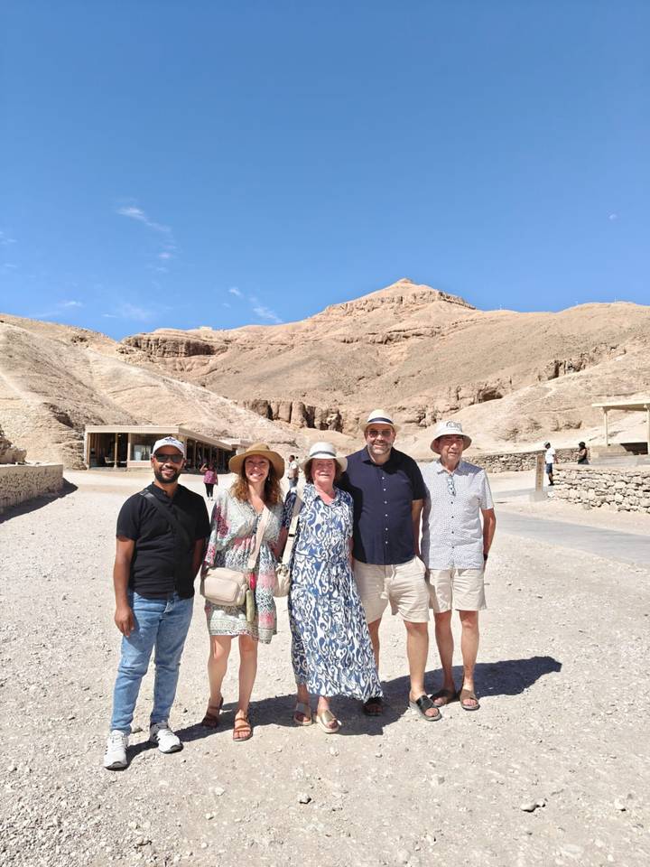 Travellers smiling in front of sun-baked cliffs and tomb entrances in Egypt's Valley of the Kings.