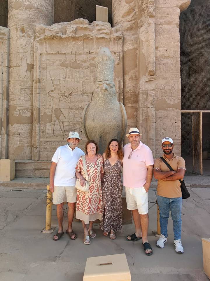 Group standing in front of a granite falcon statue at Edfu temple adorned with hieroglyphics.