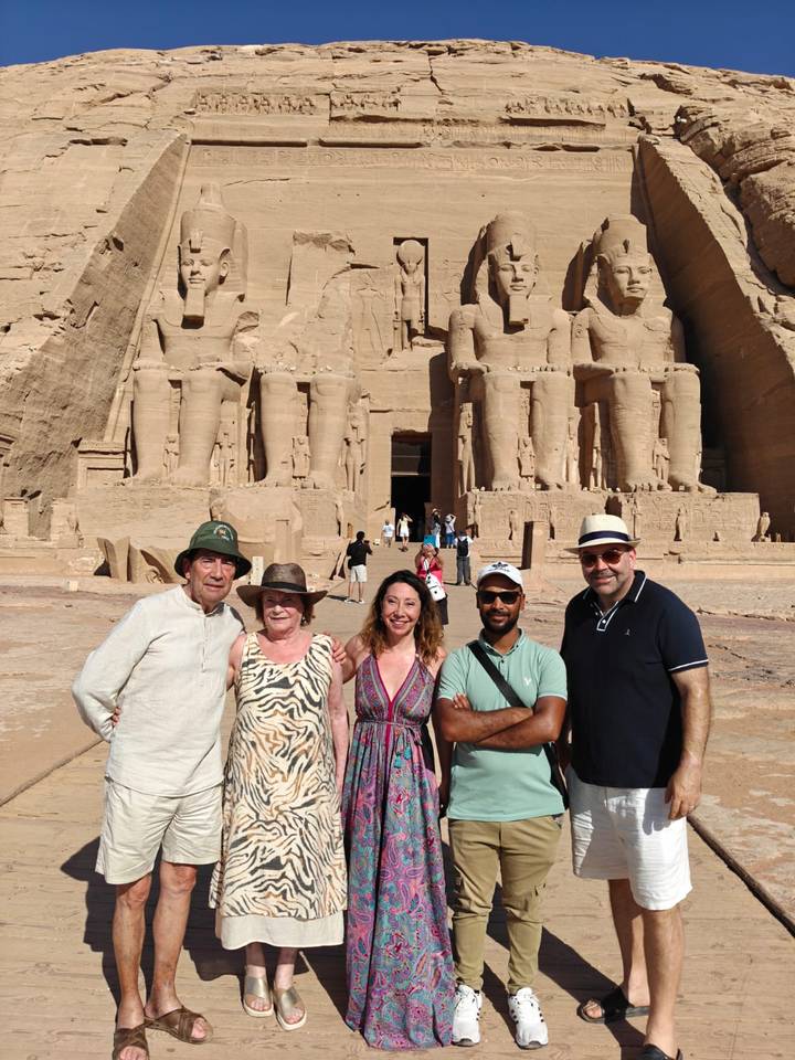 Tourists posing before the colossal statues of Abu Simbel temple under bright daylight.