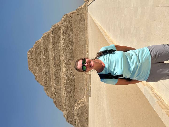 Smiling traveler stands before the ancient Step Pyramid of Djoser in a sun-baked desert complex.